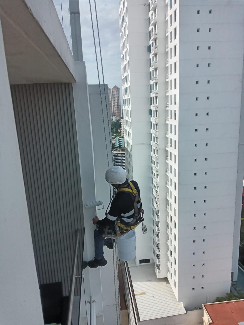 Técnico pintando una fachada con equipo de cuerdas